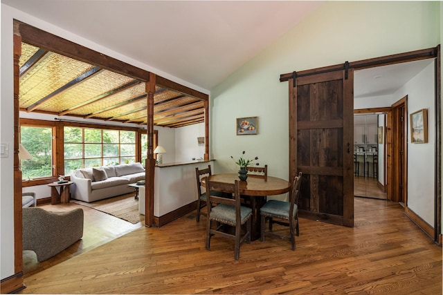 dining area featuring wood finished floors, a barn door, baseboards, and high vaulted ceiling