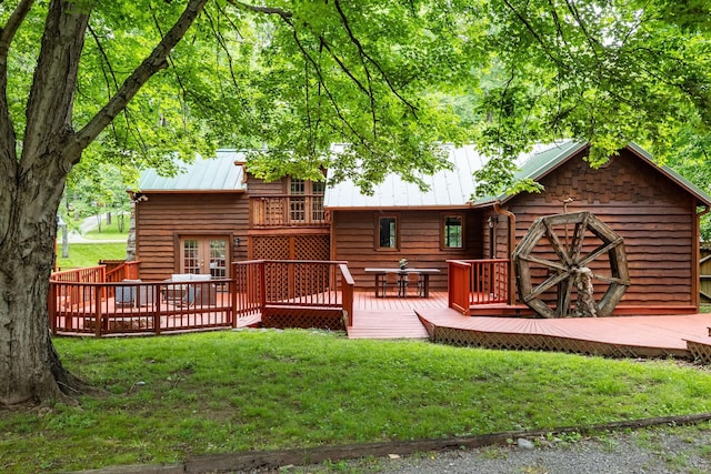 rear view of property featuring a lawn, a wooden deck, metal roof, and french doors