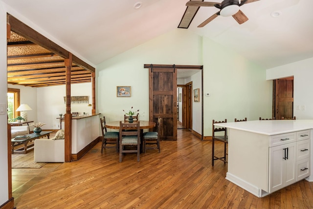 dining area featuring a barn door, a ceiling fan, light wood-type flooring, baseboards, and high vaulted ceiling