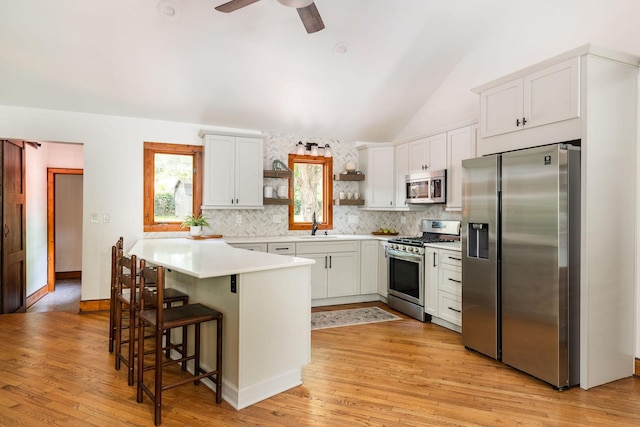kitchen with appliances with stainless steel finishes, open shelves, lofted ceiling, tasteful backsplash, and a kitchen bar