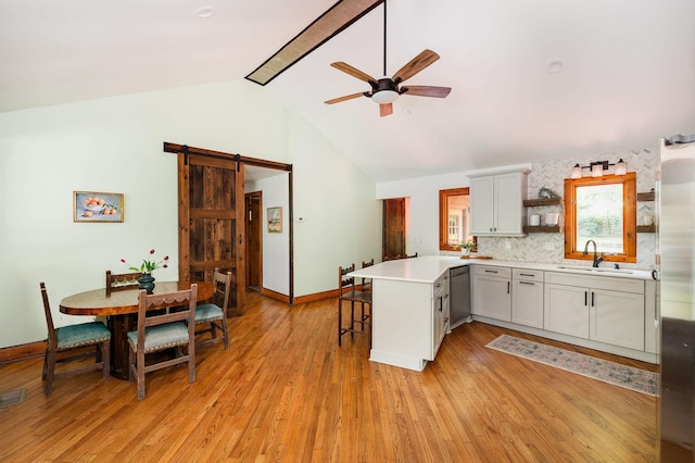 kitchen featuring a sink, stainless steel dishwasher, a barn door, a peninsula, and ceiling fan