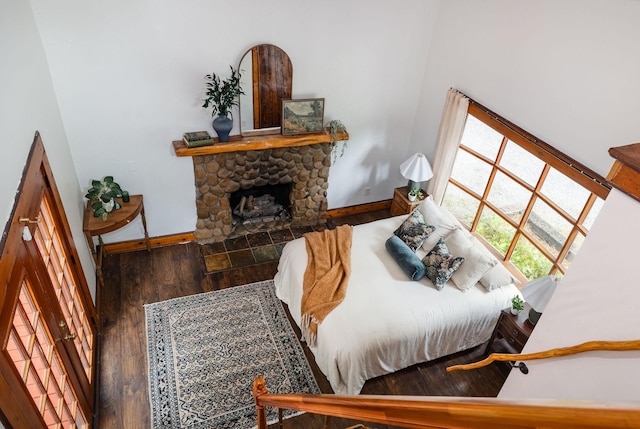 bedroom featuring baseboards, wood finished floors, and a stone fireplace