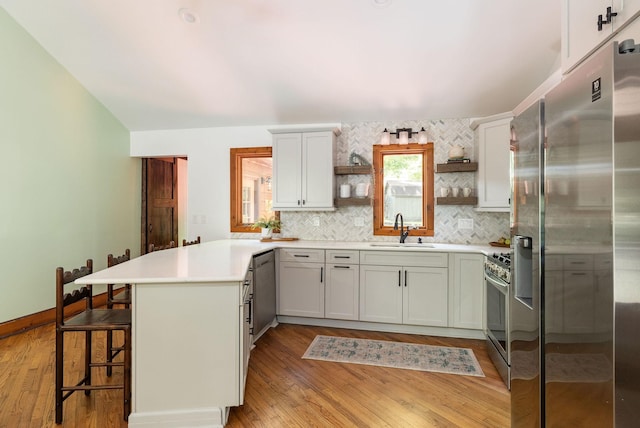 kitchen with appliances with stainless steel finishes, open shelves, a peninsula, a sink, and decorative backsplash