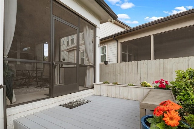 view of property exterior featuring a sunroom, a wooden deck, and fence