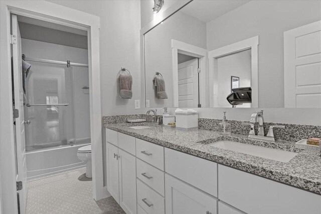 full bath with toilet, bath / shower combo with glass door, double vanity, and tile patterned flooring