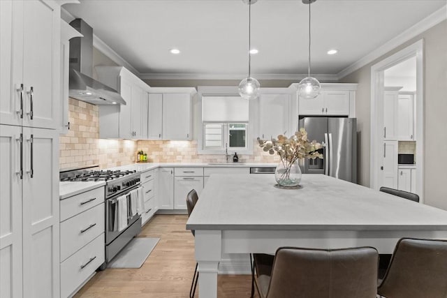 kitchen featuring appliances with stainless steel finishes, wall chimney exhaust hood, a sink, ornamental molding, and a kitchen bar