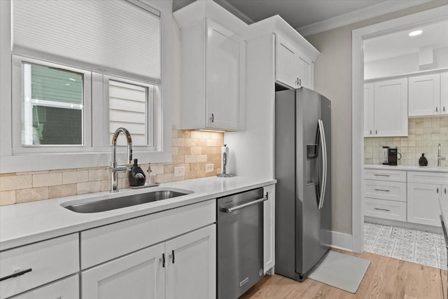 kitchen with appliances with stainless steel finishes, a sink, white cabinets, backsplash, and light countertops