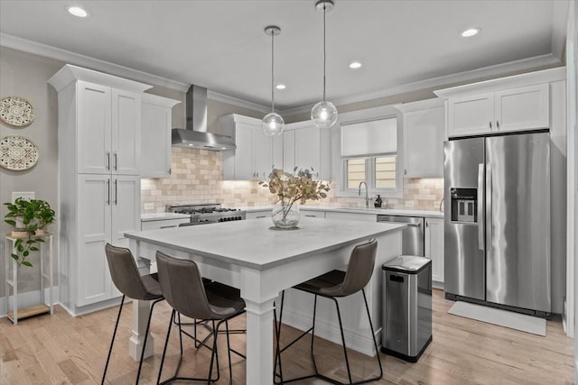 kitchen featuring wall chimney exhaust hood, stainless steel appliances, a sink, light countertops, and white cabinetry