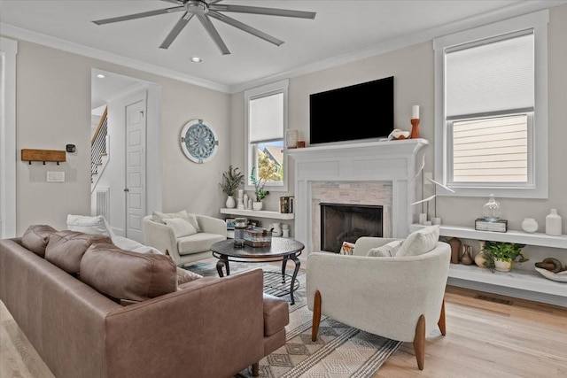 living room featuring a ceiling fan, crown molding, a high end fireplace, light wood-style flooring, and stairway