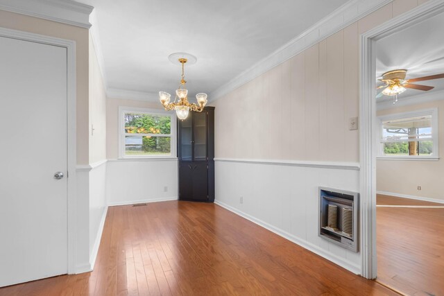 unfurnished dining area featuring plenty of natural light, a chandelier, wood finished floors, heating unit, and crown molding