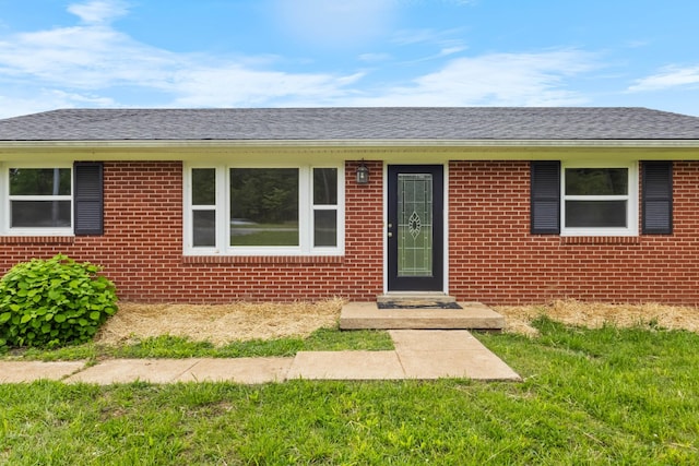 entrance to property featuring brick siding, a yard, and a shingled roof