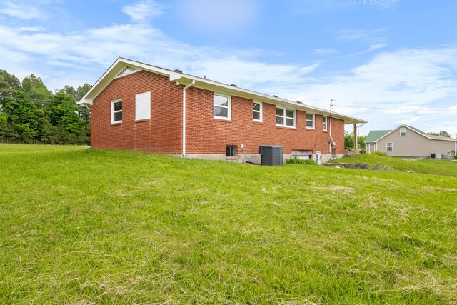 back of house featuring cooling unit, a lawn, and brick siding