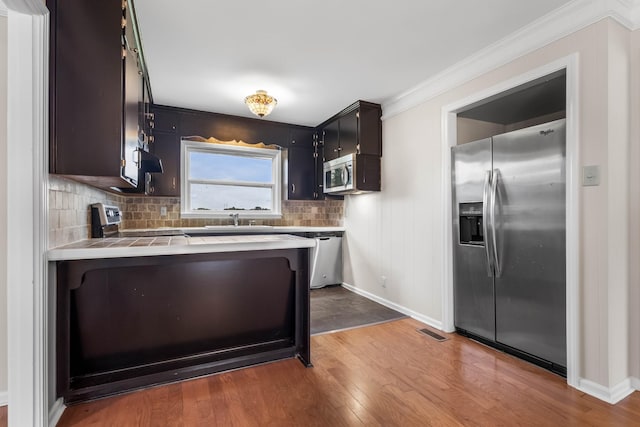 kitchen with stainless steel appliances, a sink, tile countertops, tasteful backsplash, and wood finished floors