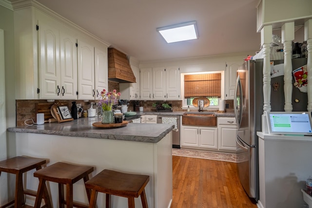 kitchen with a peninsula, a sink, custom exhaust hood, stainless steel appliances, and white cabinetry