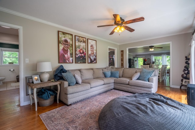living area with wood finished floors, plenty of natural light, crown molding, ceiling fan, and baseboards