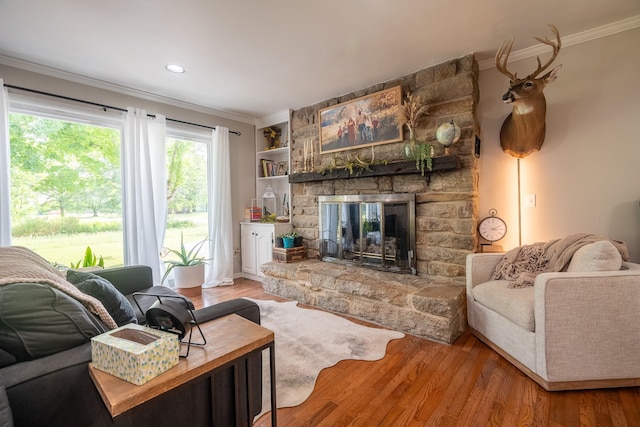 living area with ornamental molding, a stone fireplace, wood finished floors, and recessed lighting