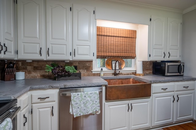 kitchen featuring appliances with stainless steel finishes, a sink, decorative backsplash, white cabinets, and ornamental molding