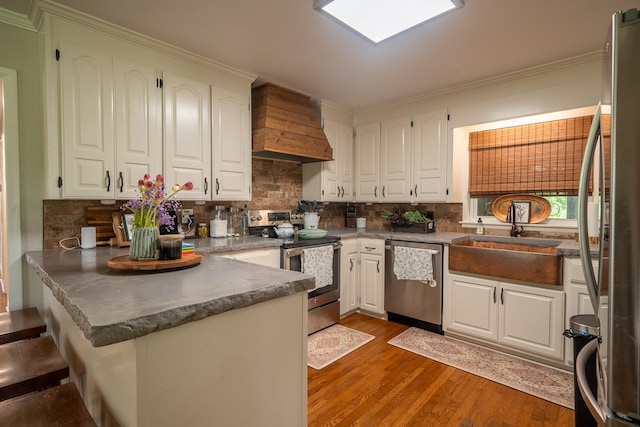 kitchen featuring appliances with stainless steel finishes, custom range hood, a peninsula, a sink, and white cabinetry