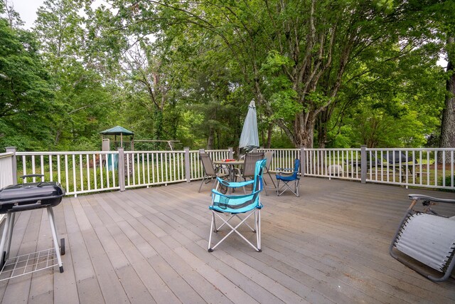 wooden deck with outdoor dining space, grilling area, and view of scattered trees