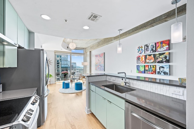 kitchen featuring a sink, appliances with stainless steel finishes, dark countertops, light wood-type flooring, and pendant lighting