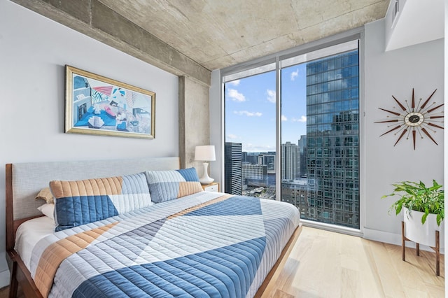 bedroom featuring wood finished floors, expansive windows, access to outside, and a city view