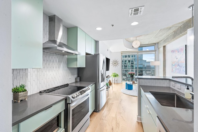 kitchen featuring stainless steel electric stove, a sink, wall chimney range hood, light wood-style floors, and backsplash