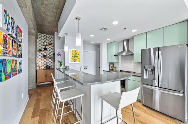 kitchen with stainless steel appliances, wall chimney exhaust hood, dark countertops, a breakfast bar area, and backsplash