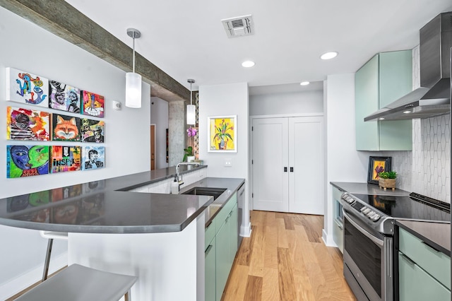 kitchen featuring stainless steel appliances, a sink, dark countertops, wall chimney range hood, and recessed lighting