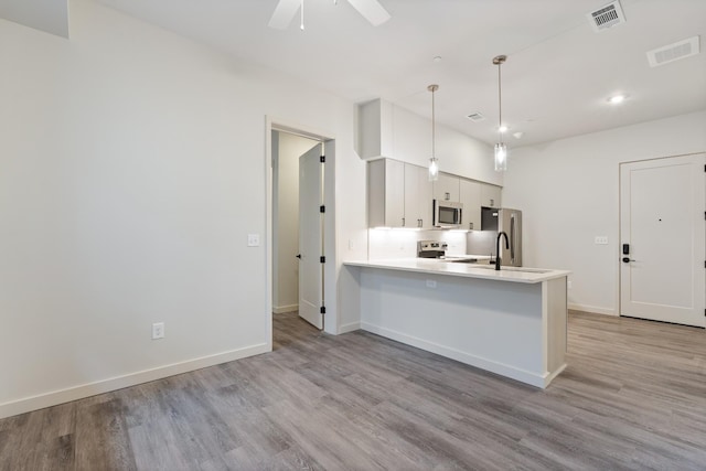 kitchen with stainless steel appliances, wood finished floors, a peninsula, light countertops, and recessed lighting