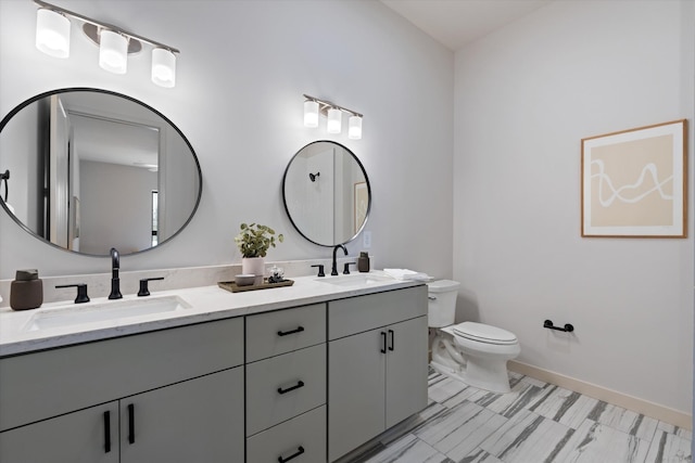 bathroom with toilet, double vanity, and baseboards