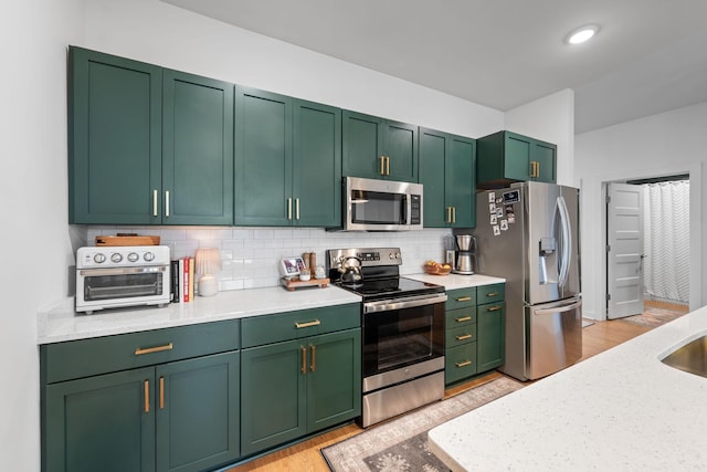 kitchen featuring appliances with stainless steel finishes, light countertops, green cabinetry, backsplash, and light wood-style flooring