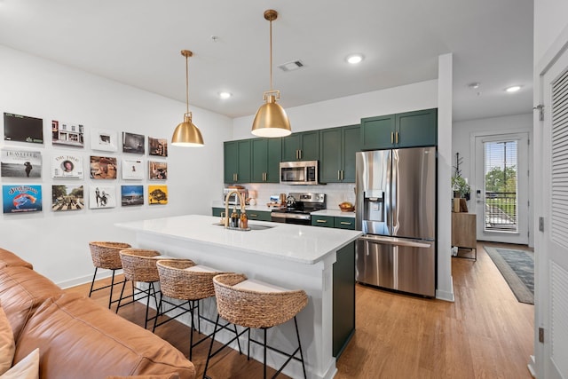 kitchen with appliances with stainless steel finishes, a sink, green cabinets, light wood-style flooring, and recessed lighting