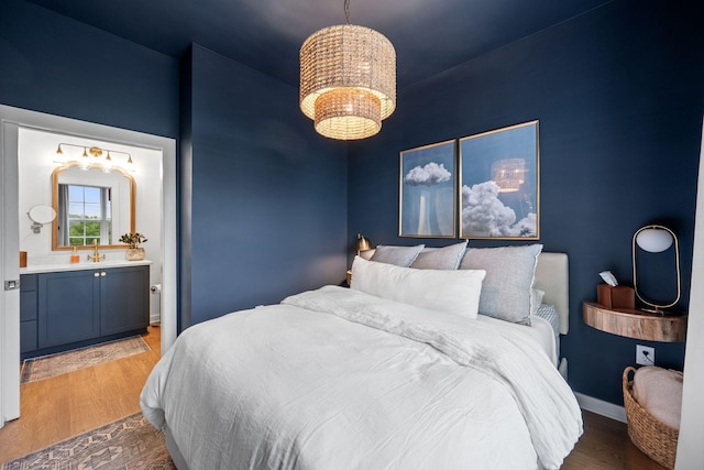 bedroom with wood finished floors, a chandelier, ensuite bathroom, a sink, and baseboards