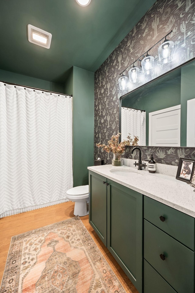 bathroom featuring wood finished floors, vanity, toilet, wallpapered walls, and curtained shower