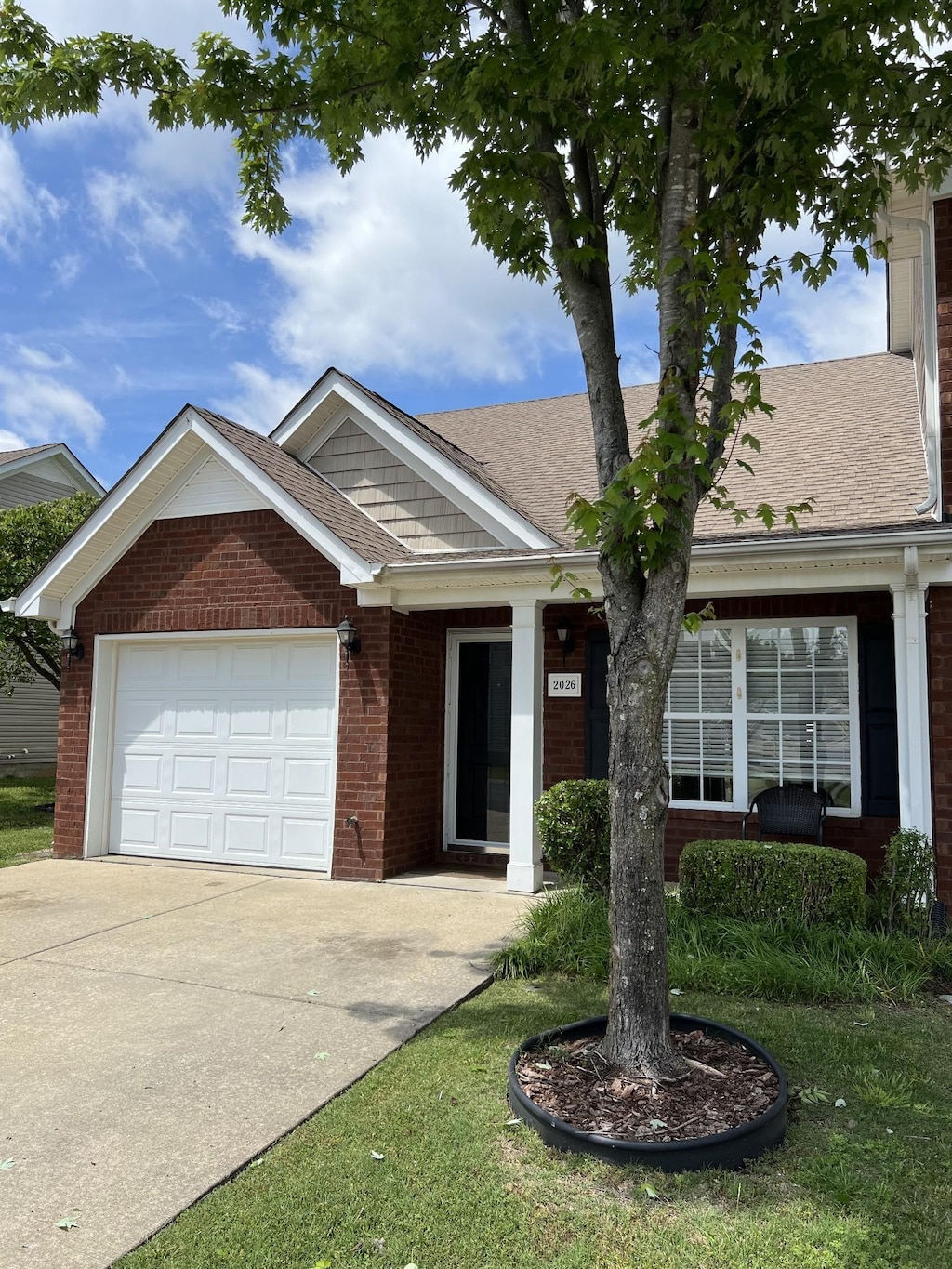 ranch-style house with brick siding, concrete driveway, an attached garage, and a shingled roof