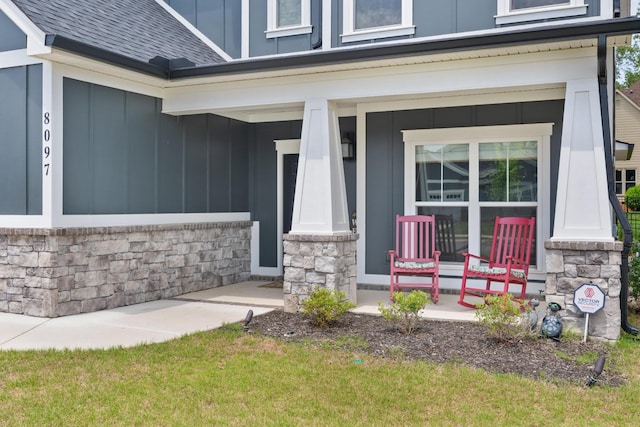 doorway to property featuring board and batten siding, covered porch, roof with shingles, and stone siding