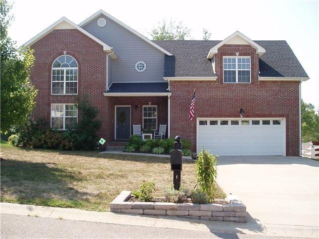 traditional-style home featuring driveway, a front lawn, a garage, and brick siding