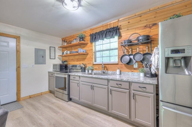 kitchen with appliances with stainless steel finishes, a sink, gray cabinets, wooden walls, and open shelves