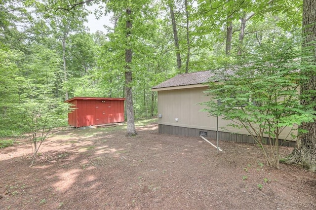 view of yard featuring a storage shed, an outdoor structure, and a view of trees