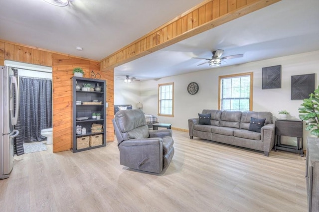 living room featuring light wood-type flooring, ceiling fan, wooden walls, and baseboards