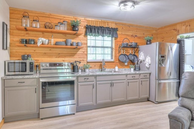 kitchen featuring stainless steel appliances, a sink, gray cabinets, wooden walls, and light wood-type flooring