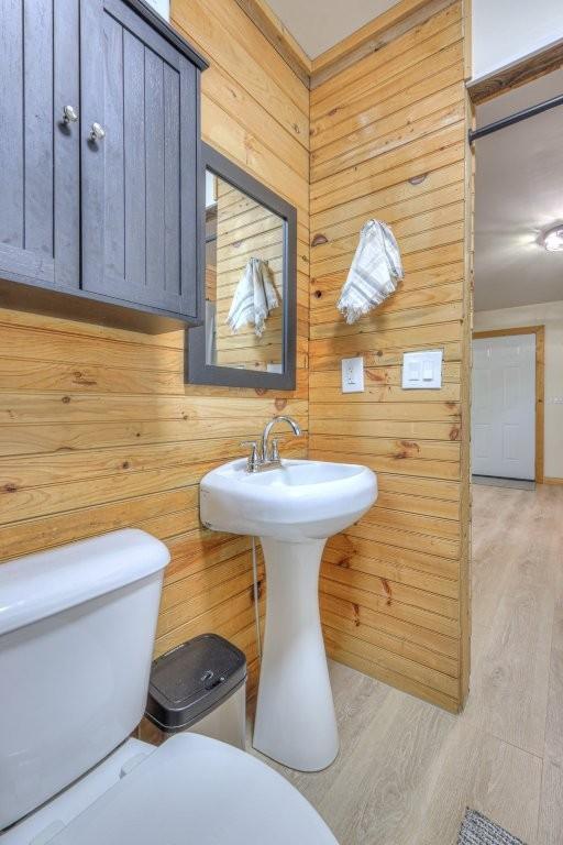 half bathroom featuring wood walls, toilet, and wood finished floors