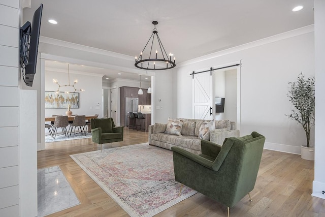 living room with a chandelier, a barn door, crown molding, baseboards, and light wood finished floors