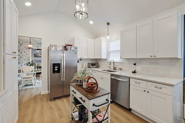 kitchen featuring stainless steel appliances, a sink, tasteful backsplash, white cabinetry, and lofted ceiling