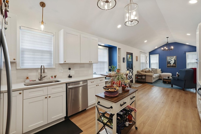 kitchen with appliances with stainless steel finishes, a sink, lofted ceiling, white cabinets, and backsplash