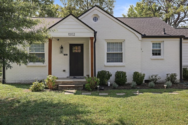 view of front facade with brick siding, roof with shingles, and a front lawn
