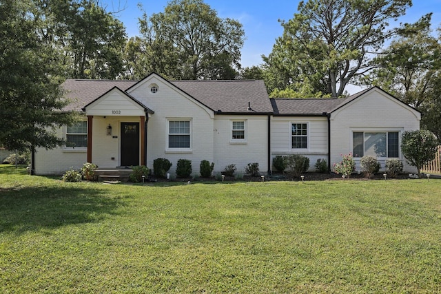 ranch-style home featuring a front yard, brick siding, and roof with shingles
