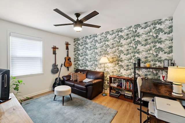 living room with wallpapered walls, ceiling fan, wood finished floors, an accent wall, and an office area