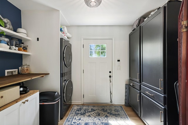 laundry area featuring cabinet space, stacked washer / drying machine, light wood finished floors, and baseboards