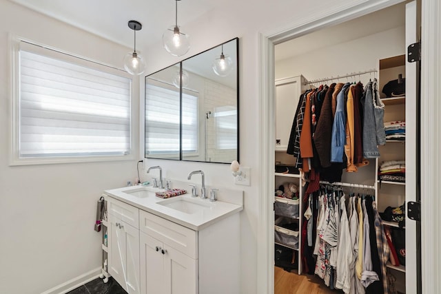 bathroom featuring double vanity, a walk in closet, and baseboards
